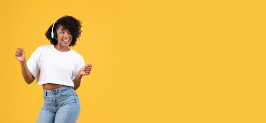 Cheerful millennial black woman in casual and wireless headphones dancing, enjoy listening music