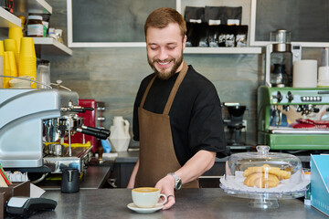 Portrait of barista male in an apron with freshly prepared cappuccino coffee