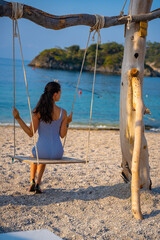 Young woman on wooden swing on Oludeniz beach. Summer holiday in Oludeniz, Turkey. Girl ride on a swing on sea coast, clear water. Travel concept