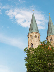 Fototapeta na wymiar Two medieval towers of St.Martini church against the blue sky and green tree. Sights of Braunschweig, Germany. Vertical photo with elements of historical buildings.