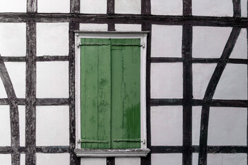 eine Fachwerkwand mit einem geschlossenen grünen Klappfensterladen aus Holz