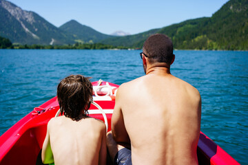 Boy with father on red boat on sky blue lake in summer in Tyrol, Austria 