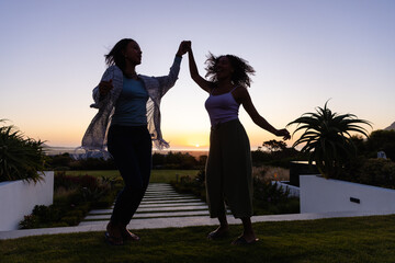 Happy biracial lesbian couple dancing in garden at sunset