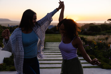 Happy biracial lesbian couple dancing in garden at sunset
