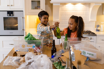 Happy biracial brother and sister sorting rubbish for recycling in kitchen - Powered by Adobe