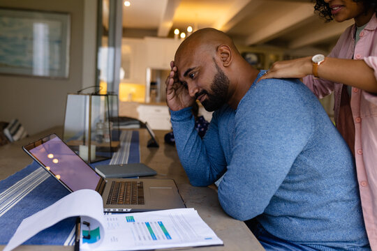 Worried biracial couple using laptop and looking at bills in dining room, copy space - Powered by Adobe