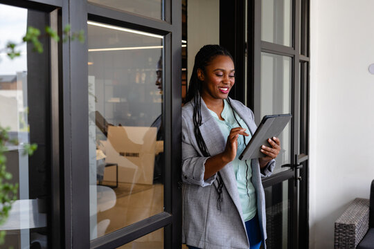 Happy plus size african american casual businesswoman using tablet in office window - Powered by Adobe