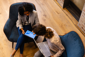 Diverse female colleagues in discussion using laptop and tablet in casual office meeting