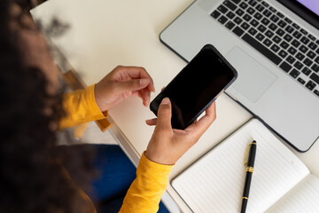Hands of biracial woman using smartphone and laptop at home