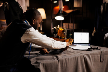 Precise craftmanship in tailoring studio by african american suitmaker cutting sartorial fabric...