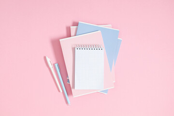 Back to school concept. Flat lay top view of stack of notepads with empty space for text, pens and pencil on isolated pastel pink background.