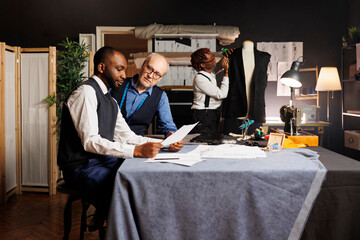 African american seamstress doing needlework on sartorial garment while tailoring coworkers sketch final outfit design. Master couturier and apprentices working on custom menswear fashion collection