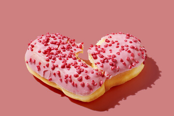 Bitten heart shaped donut with glaze on pink pastel background