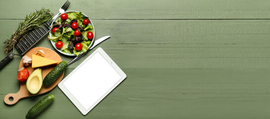 Tablet computer, plate with fresh salad and different products on green wooden background with space for text