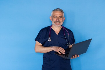 Obraz na płótnie Canvas Middle aged european man wearing medical workwear and eyeglasses doctor holding laptop over blue studio background