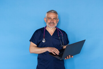Obraz na płótnie Canvas Middle aged european man wearing medical workwear and eyeglasses doctor holding laptop over blue studio background
