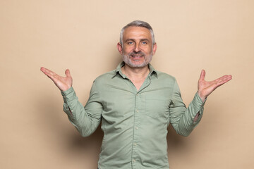 Elderly man shrugging shoulders looking puzzled spread hands isolated on beige background