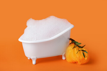 Small bathtub with foam, sponge and eucalyptus branch on color background