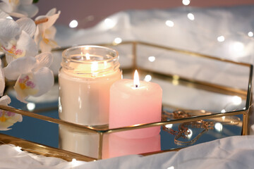 Tray with burning candles and flowers on white fabric, closeup