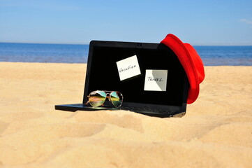 Tourism, black laptop and sunglasses on a sandy beach. Relax on the seashore.