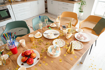 Dining table with Birthday cake, treats, champagne and party hats in kitchen