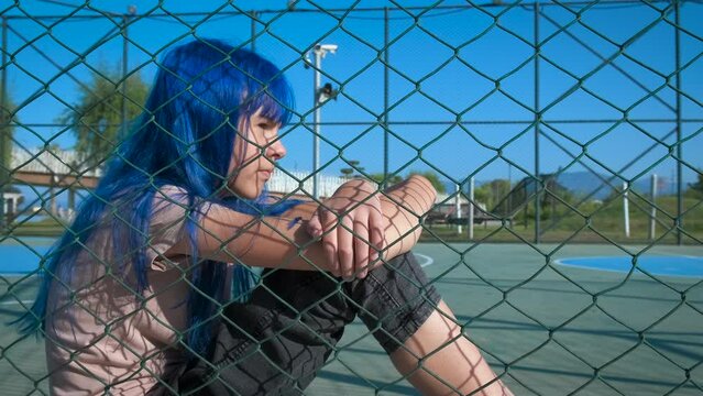Difficult relationships in adolescence. A view of young girl with difficulties sits on the sport ground and suffer from loneliness in the day light.