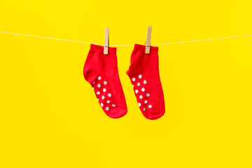 Pair of red cotton socks hanging on rope against yellow background