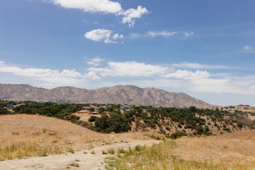 A beautiful American landscape with mountains, trees, and country houses in California on sunny days with blue sky. Bakersfield, California, USA - 7-22-2021