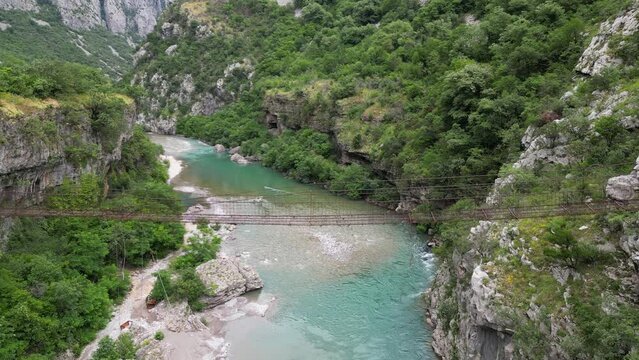 Suspension bridge in the middle of a beautiful rocky canyon with a turquoise river. Aerial view. Moraca river canyon. Montenegro.
