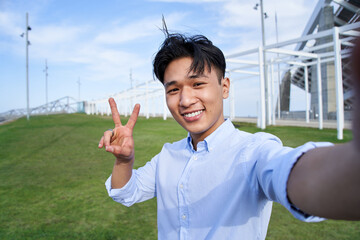 Selfie portrait looking at camera of Asian teenage boy making peace sign. Smiling attractive young...