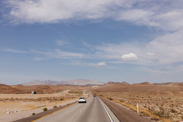 A beautiful asphalt road among hills with dry grass. A scenic landscape with highway, mountains on background and blue sky with fluffy clouds on sunny day. Bakersfield, California, USA - 7-22-2021