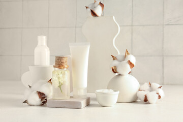 Composition with cosmetic products, plaster stands and cotton flowers on table against light tile background