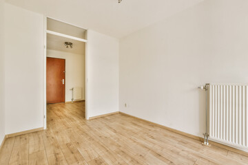 an empty room with white walls and wood flooring on the right side, there is a rad door in the left corner
