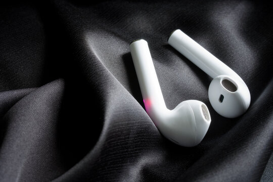 A pair of white TWS earphones among black silk. The concept of the noise reduction function in modern audio equipment and tws headphones. Photo. Selective focus.