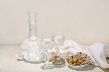Shots and decanter of cold vodka with snacks on light background