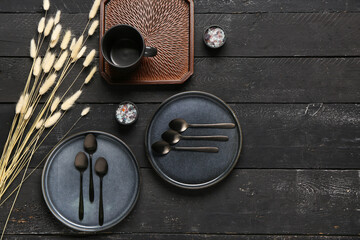 Clean plates with set of spoons and dried lagurus on black wooden table - obrazy, fototapety, plakaty