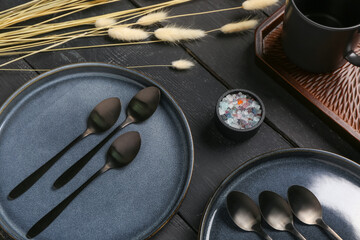 Clean plates with set of spoons and dried lagurus on black wooden table