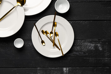 Clean plates with set of golden cutlery on black wooden table