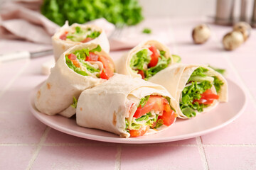 Plate of tasty lavash rolls with tomatoes and greens on pink tile background