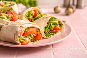 Plate of tasty lavash rolls with tomatoes and greens on pink tile background