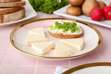 Plate with triangles of tasty processed cheese, bread pieces and vegetables on pink tile background, closeup