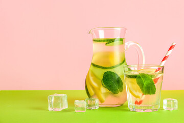 Jug and glass of lemonade with cucumber on green table