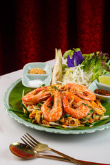 TTaste the Essence of Thailand: Exquisite Pad Thai, a Popular Traditional Dish with Silky Noodles, Succulent Shrimp, and a Burst of Sweet and Sour Flavors on a Ceramic Plate red Thai Art Curtain
