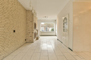 a long hallway with white tile on the floor and beige brick wall behind it, there is an open door...