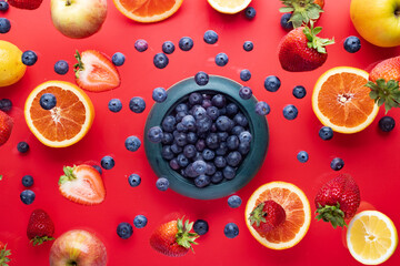 pot with levitating blueberries, strawberries and oranges on a red background. View from above.