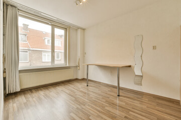 an empty room with wood flooring and white paint on the walls, there is a small table in front of the window