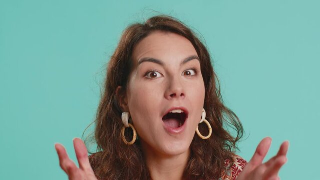 Oh my God, Wow. Excited amazed winner woman raising hands in surprise looking at camera with big eyes, shocked by sudden victory. Sincere attractive girl isolated alone on blue studio background