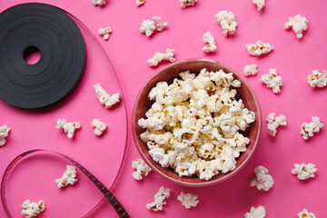 Obraz na płótnie Canvas Bowl with tasty popcorn and film reel on pink background