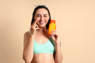 Young woman with sunscreen cream on beige background