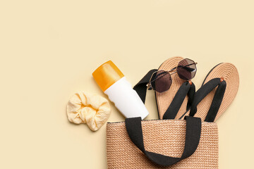 Wicker bag with sunglasses, flip flops and bottle of sunscreen cream on pale yellow background